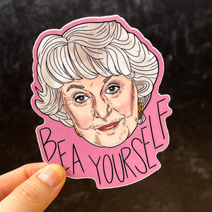 A sticker featuring Bea Arthur and the message "Bea Yourself" is held up against a black background