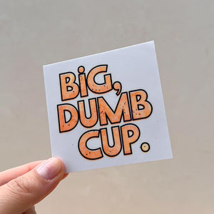 A big, dumb cup sticker is held lovingly against a white background that you totally can't tell is my backyard, right?