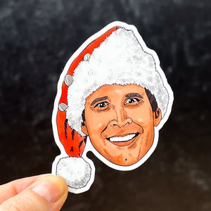 A portrait sticker of Clark from Christmas Vacation held against a black background. He's wearing a Santa hat and a smile that says "residuals forever."