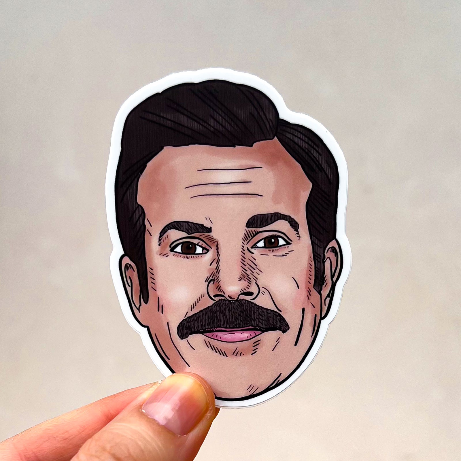 An illustrated Ted Lasso sticker held against a white background